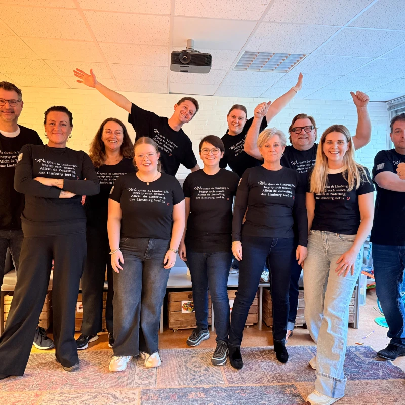 groep volwassenen in zwarte t-shirts van ton meisen poseert lachend voor camera